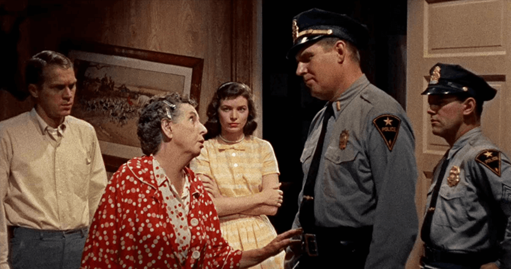Two policeman question an elderly woman in a robe, while a male and female teenager stare in disbelief.