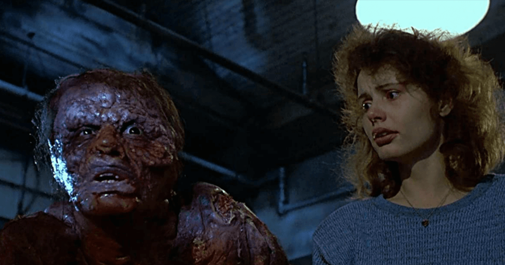 A hideously deformed man stands next to a woman who looks concerned.