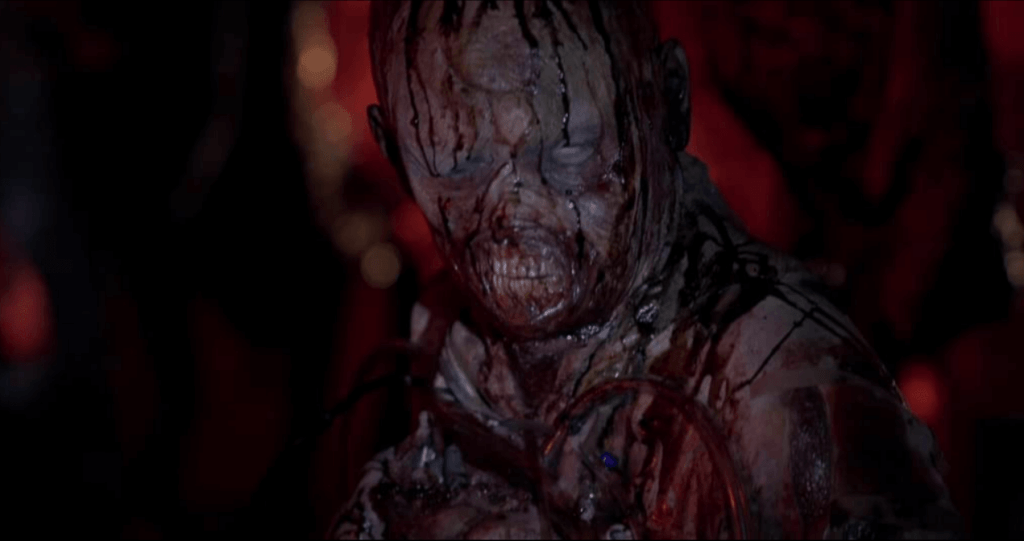 A deformed humanoid creature covered in tentacles and blood marches forward. First-person point of view.